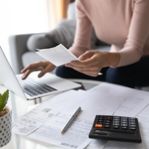 Woman working on laptop with papers and calculator